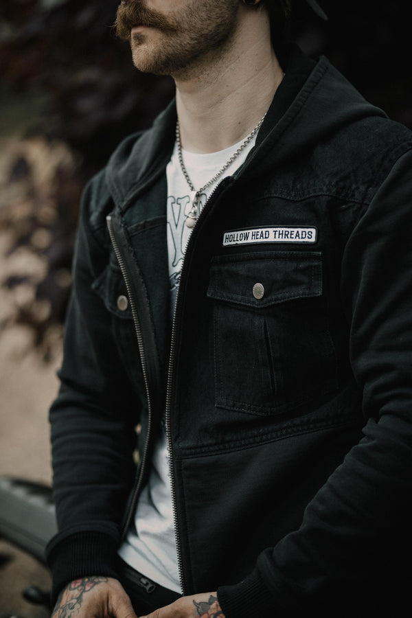Person wearing a black jacket with 'Hollow Head Threads' label, blurred background